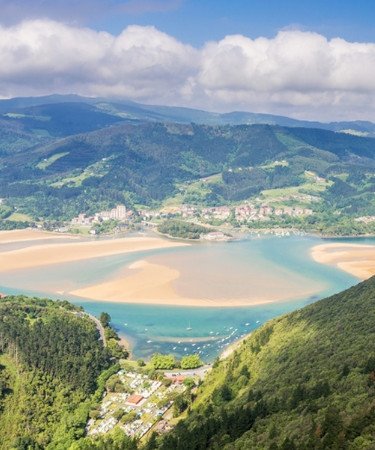 Vista panorámica de la playa de Laida desde lo alto de una montaña, mostrando su extensa arena en marea baja.